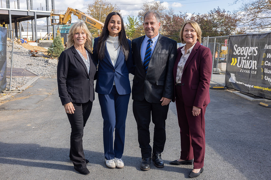 Four people in suits pose for a photo in a parking lot